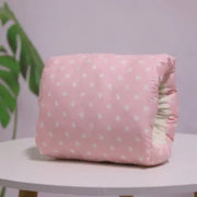 Pink cushion with white floral pattern on a white surface with a blurred green plant in the background