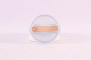 Clear container with a gold-colored object on a light purple background