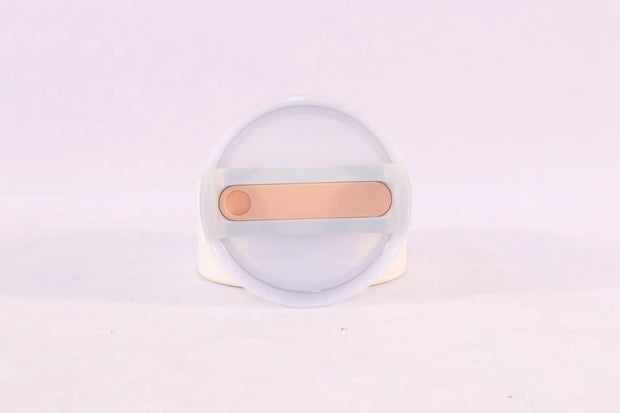 Clear container with a gold-colored object on a light purple background