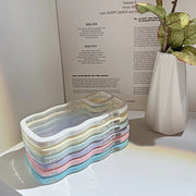 Stack of colorful phone cases on a white surface with a plant and a book in the background