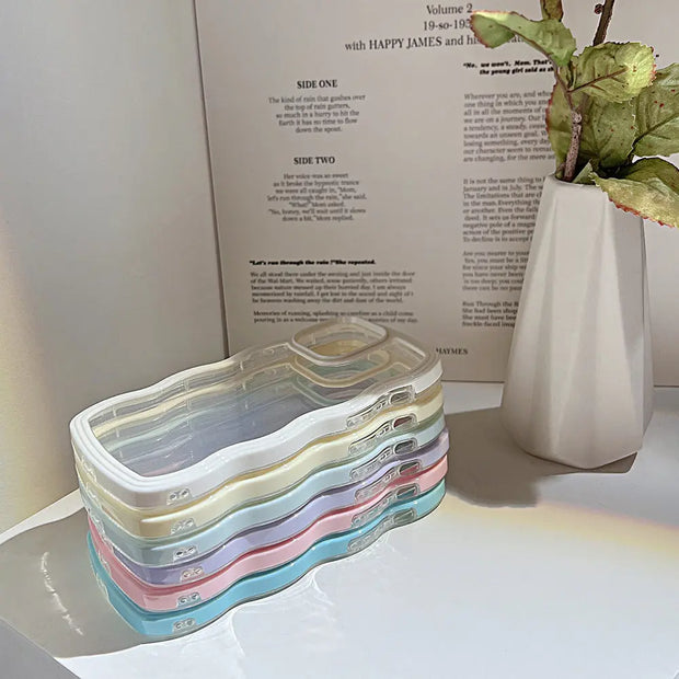 Stack of colorful phone cases on a white surface with a plant and a book in the background